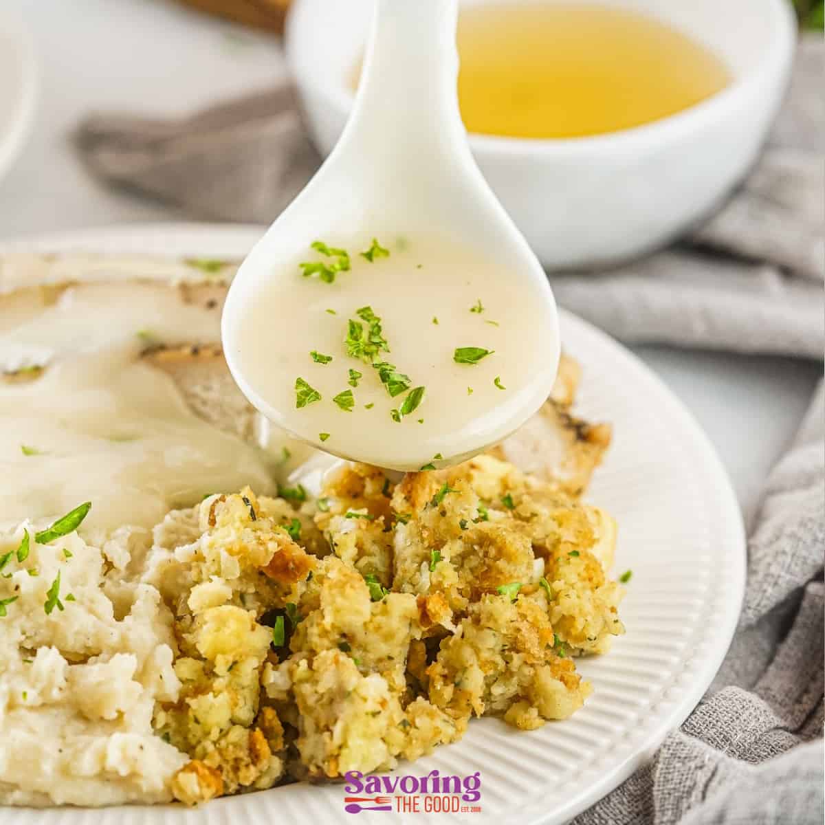 A spoon is pouring turkey gravy with drippings over a plate of mashed potatoes and stuffing.