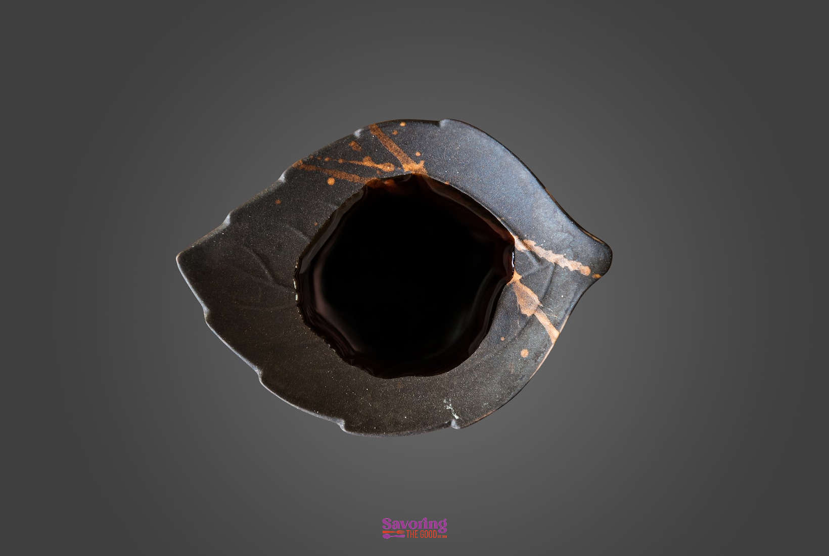 soy sauce in a black leaf shaped bowl on a dark background.