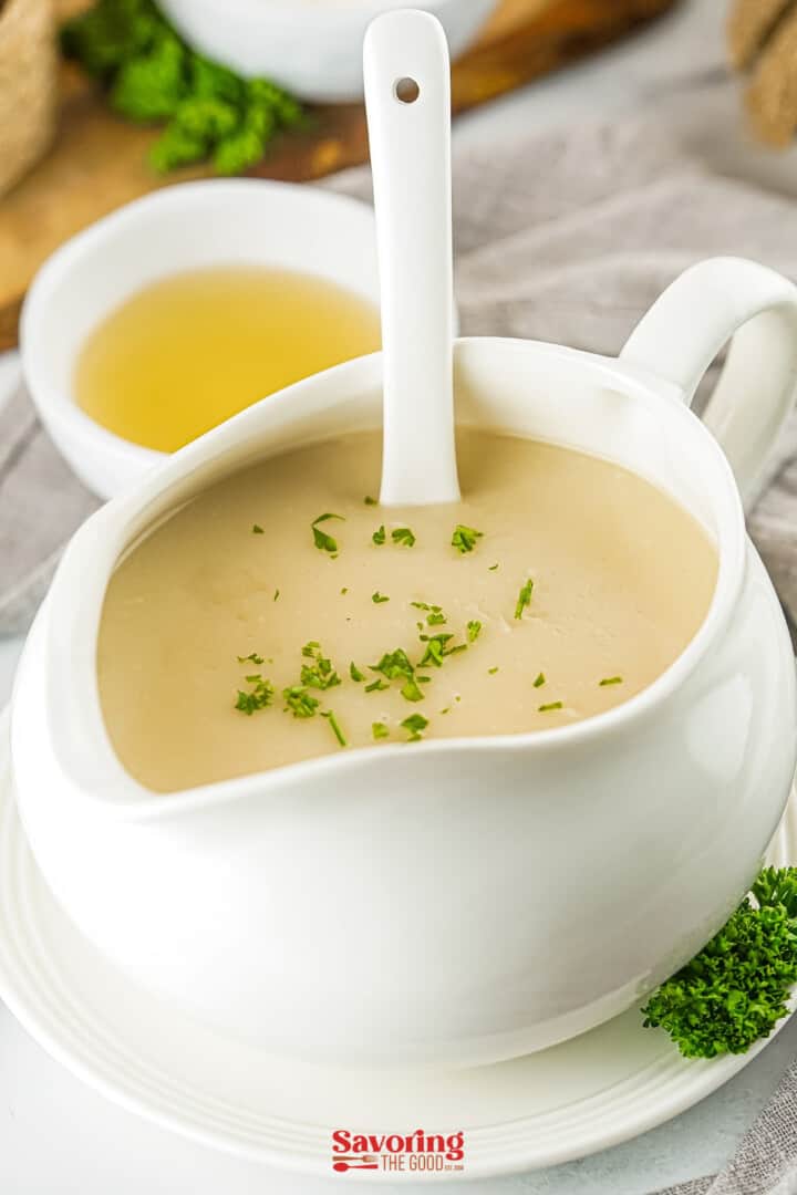 A white bowl of soup with a spoon on top, filled with delicious turkey gravy from drippings.