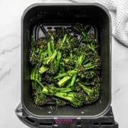 Broccoli in an air fryer on a marble countertop.