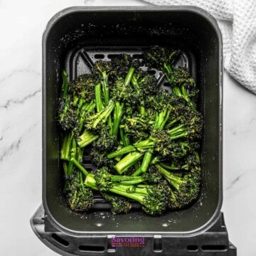 Broccoli in an air fryer on a marble countertop.