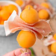 A person is holding melon wrapped in prosciutto.