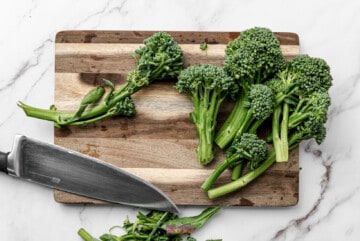 Fresh broccolini on a cutting board with a knife.
