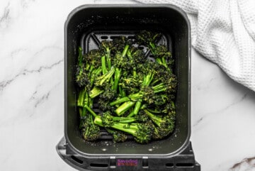 A tray of broccolini roasted in a air fryer basket.