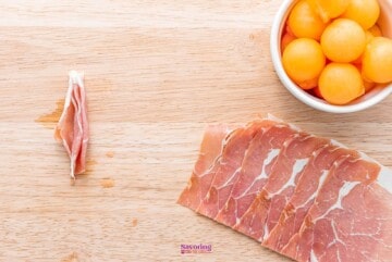 Sliced ham and melon on a wooden table.