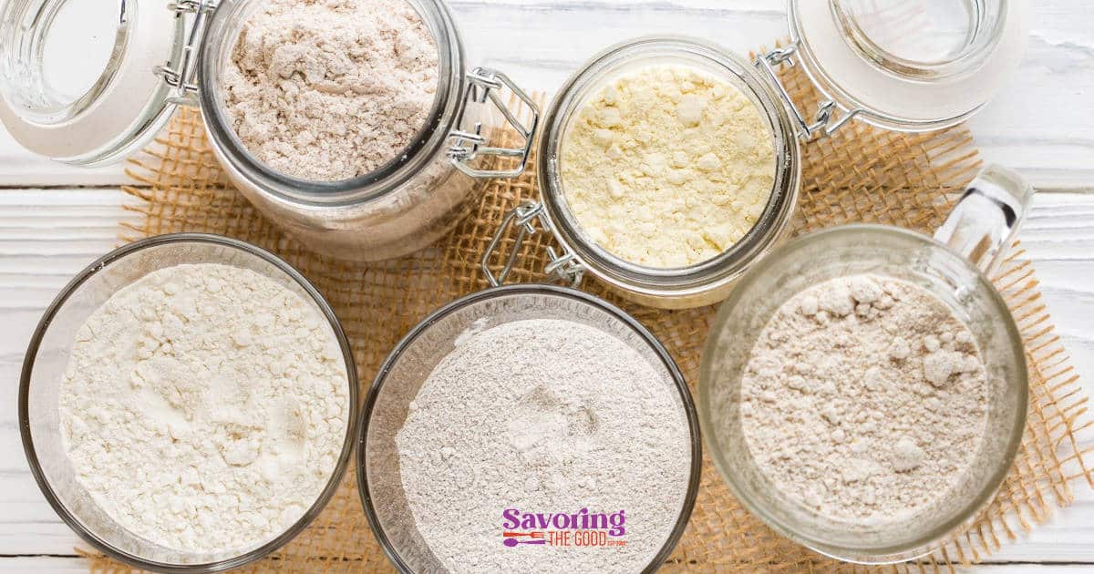 Different types of flour in jars on a wooden table.