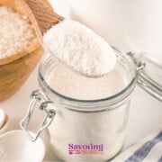White rice flour in a glass jar next to a spoon and spoons.
