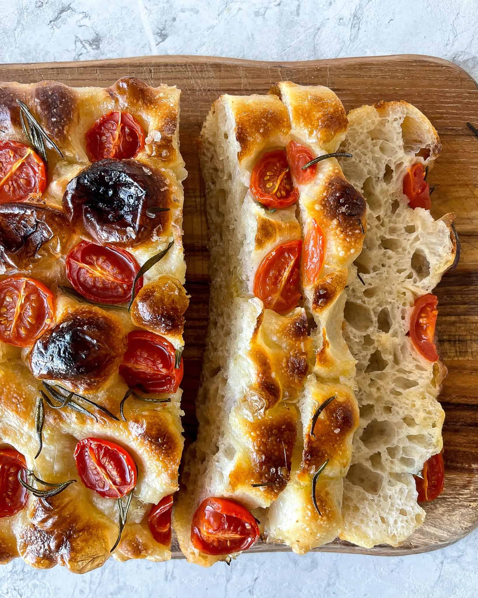 A loaf of bread with tomatoes and rosemary on a cutting board.