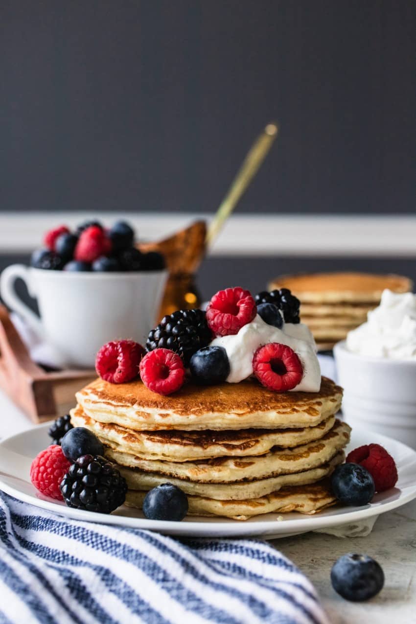 A stack of pancakes with berries and whipped cream.