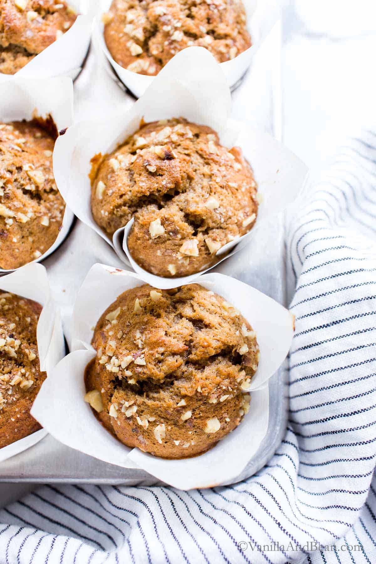 Oatmeal muffins in a muffin tin on a white tablecloth.