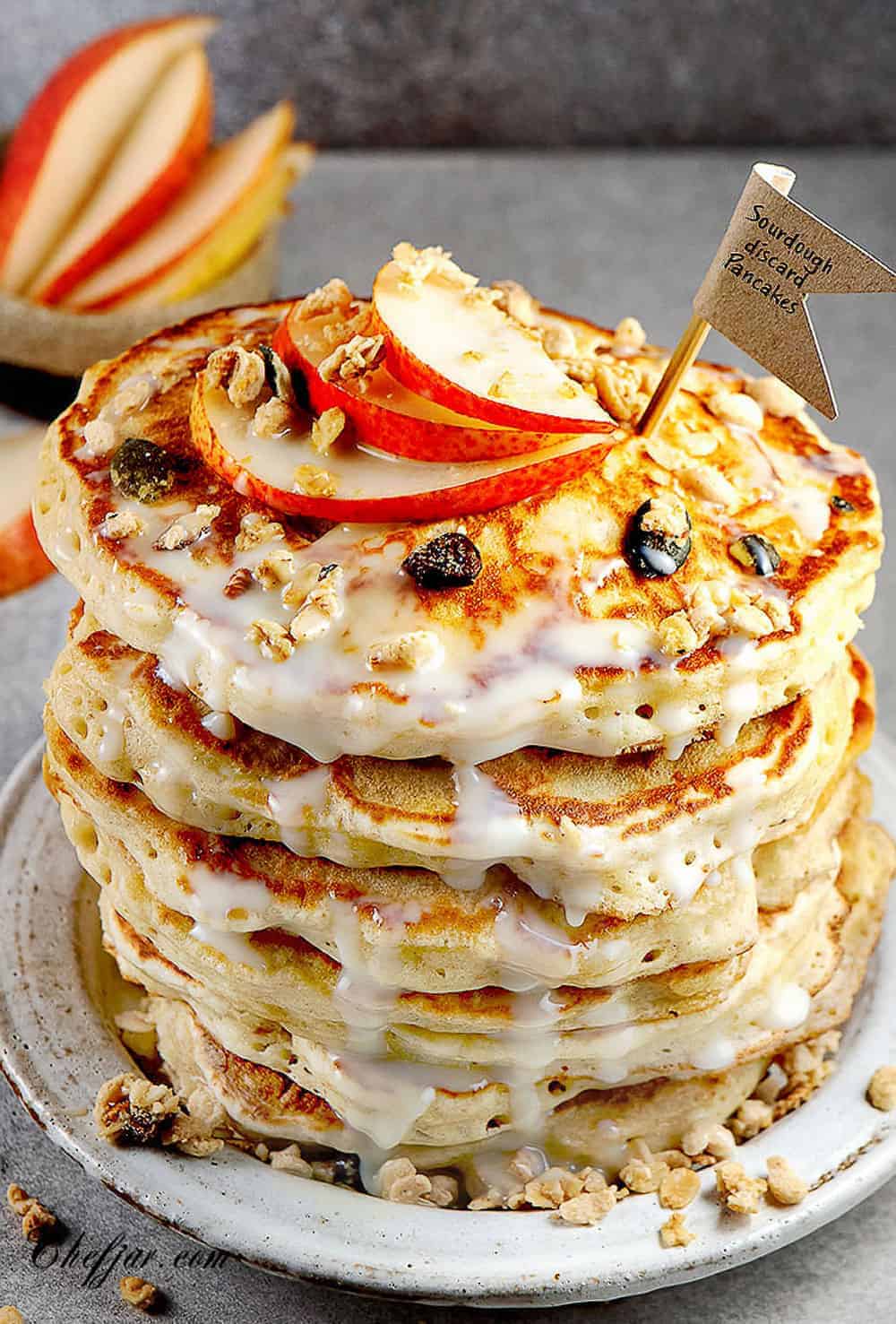 A stack of pancakes with icing and apples.