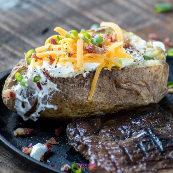 A steak and a baked potato on a black plate.