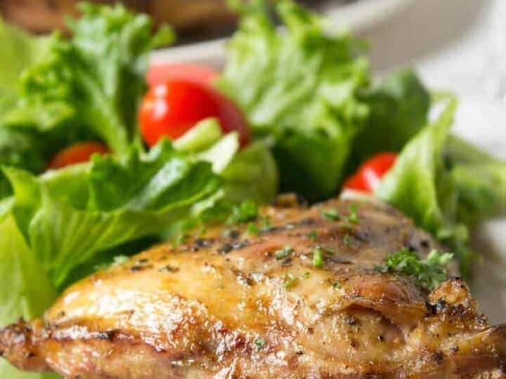 Grilled chicken breasts on a white plate with a salad.