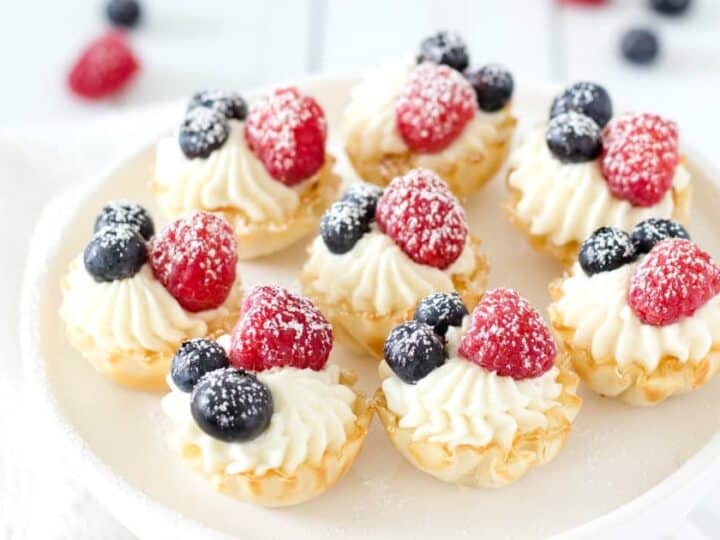 Mini tarts with berries and cream on a white plate.