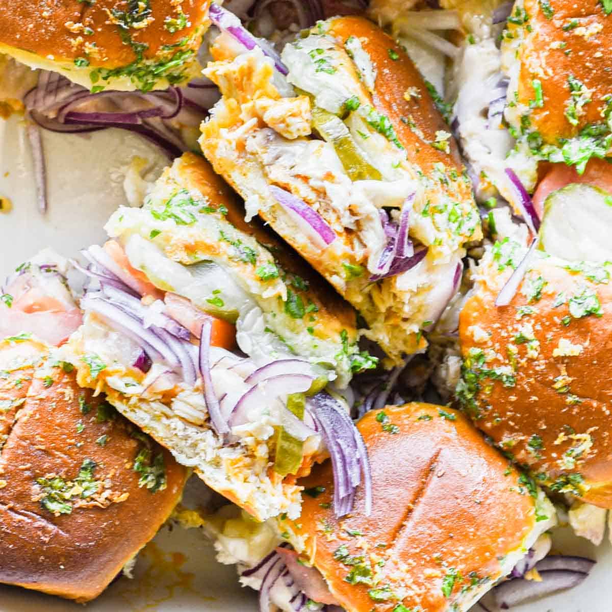 A plate of sliders with onions, lettuce, and pickles.