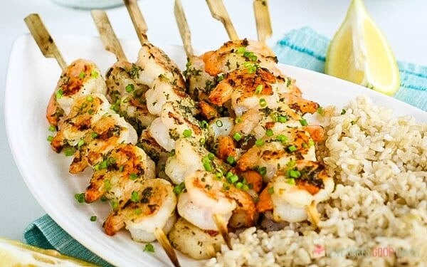 Shrimp skewers on a plate with rice and lemons.
