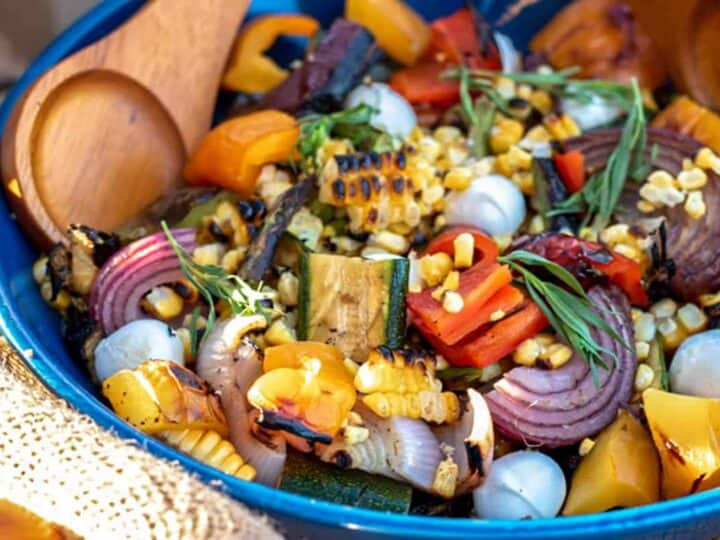 Grilled vegetables in a blue bowl with a wooden spoon.