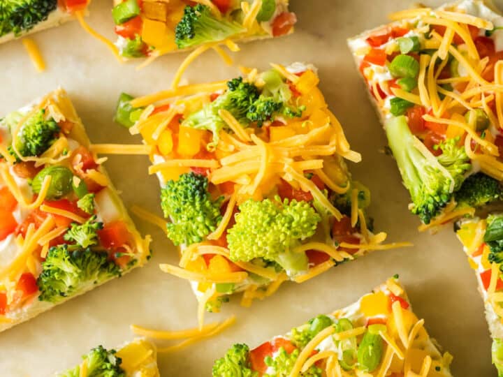 A tray of broccoli and cheese pizzas on a baking sheet.