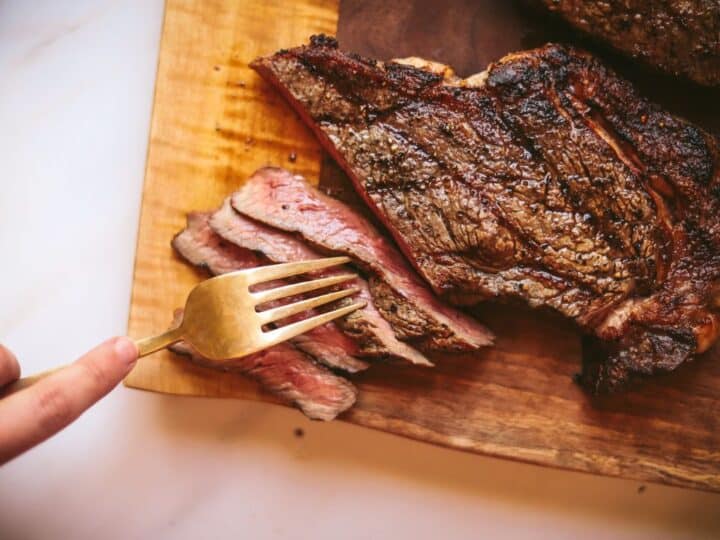 A person cutting a steak with a fork on a cutting board.