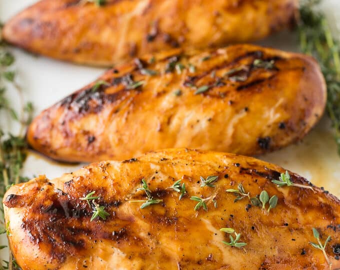 Grilled chicken breasts on a white plate with herbs.