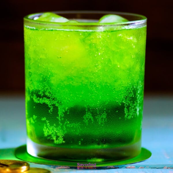 A chilled glass of green beverage with ice cubes.