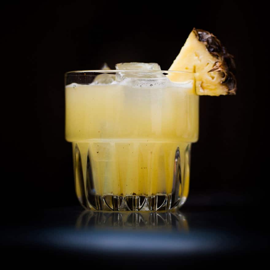 A glass with a drink and a slice of pineapple on top.