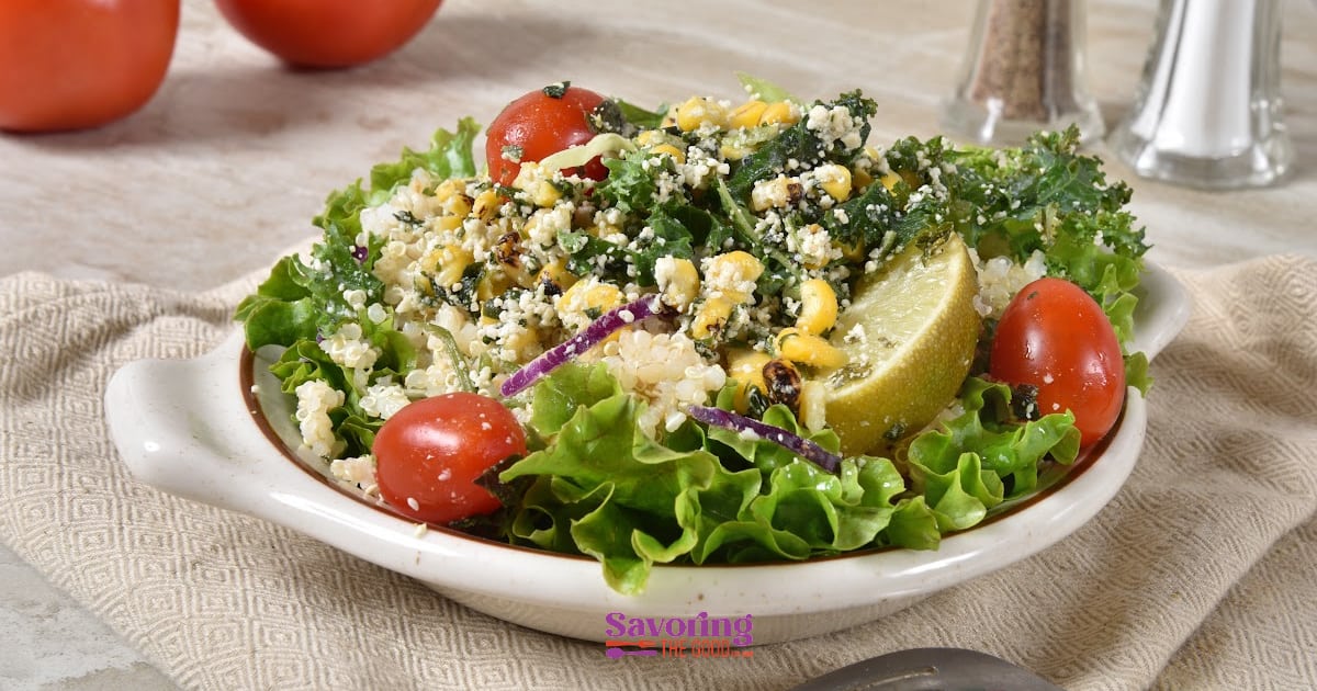 A fresh salad with leafy greens, tomatoes, crumbled cheese, red onion, and lemon on a plate.
