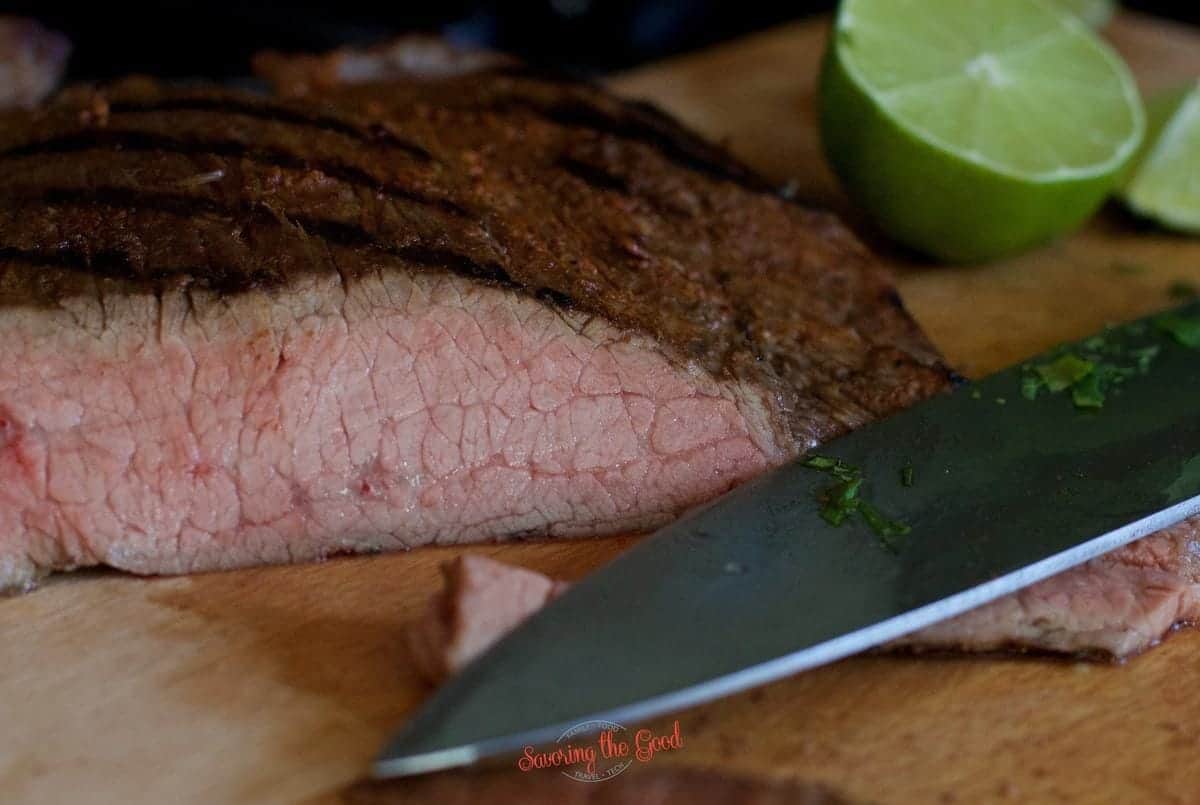 Sliced sous vide flank steak on a cutting board with a knife and lime wedge.