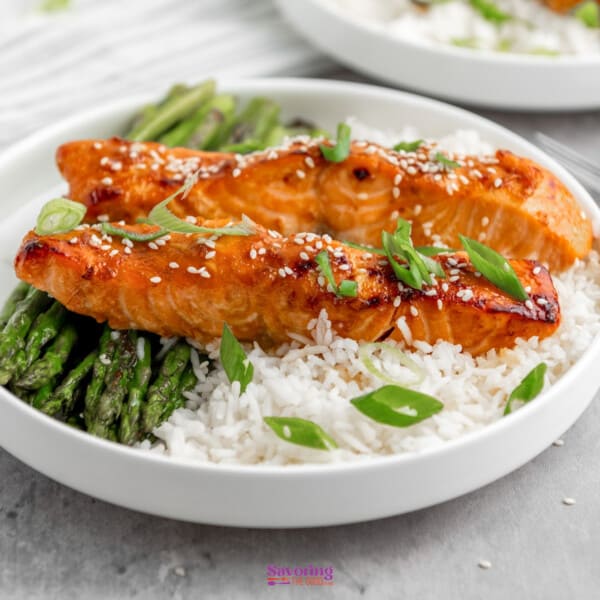 Air fryer Glazed salmon fillet over a bed of rice with asparagus on the side, garnished with sesame seeds and green onions.
