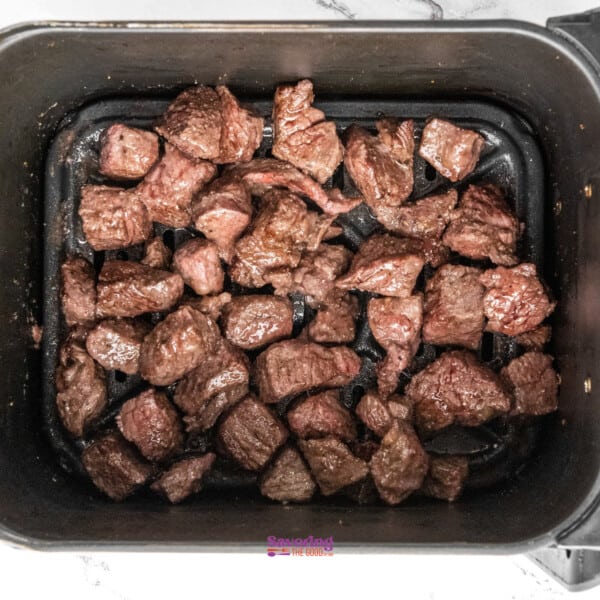 Cubed beef pieces seared in a black air fryer basket.