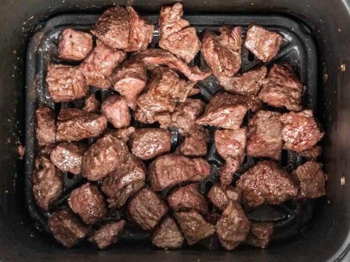 Cubed beef pieces seared in a black air fryer basket.