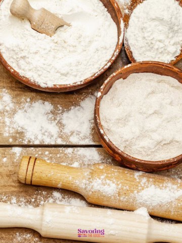 Bowls of flour with a rolling pin on a wooden surface, suggesting baking preparation.
