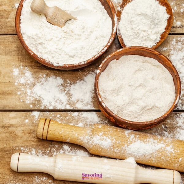 Bowls of flour with a rolling pin on a wooden surface, suggesting baking preparation.