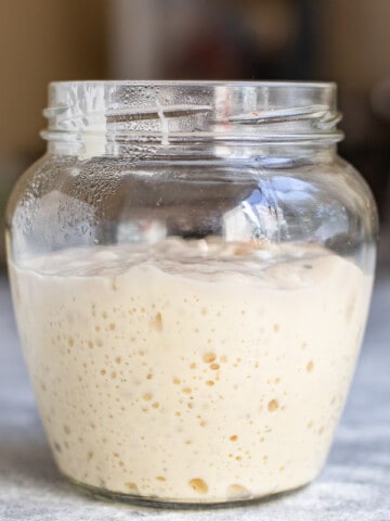 A glass jar containing active sourdough starter with visible bubbles on a kitchen countertop.