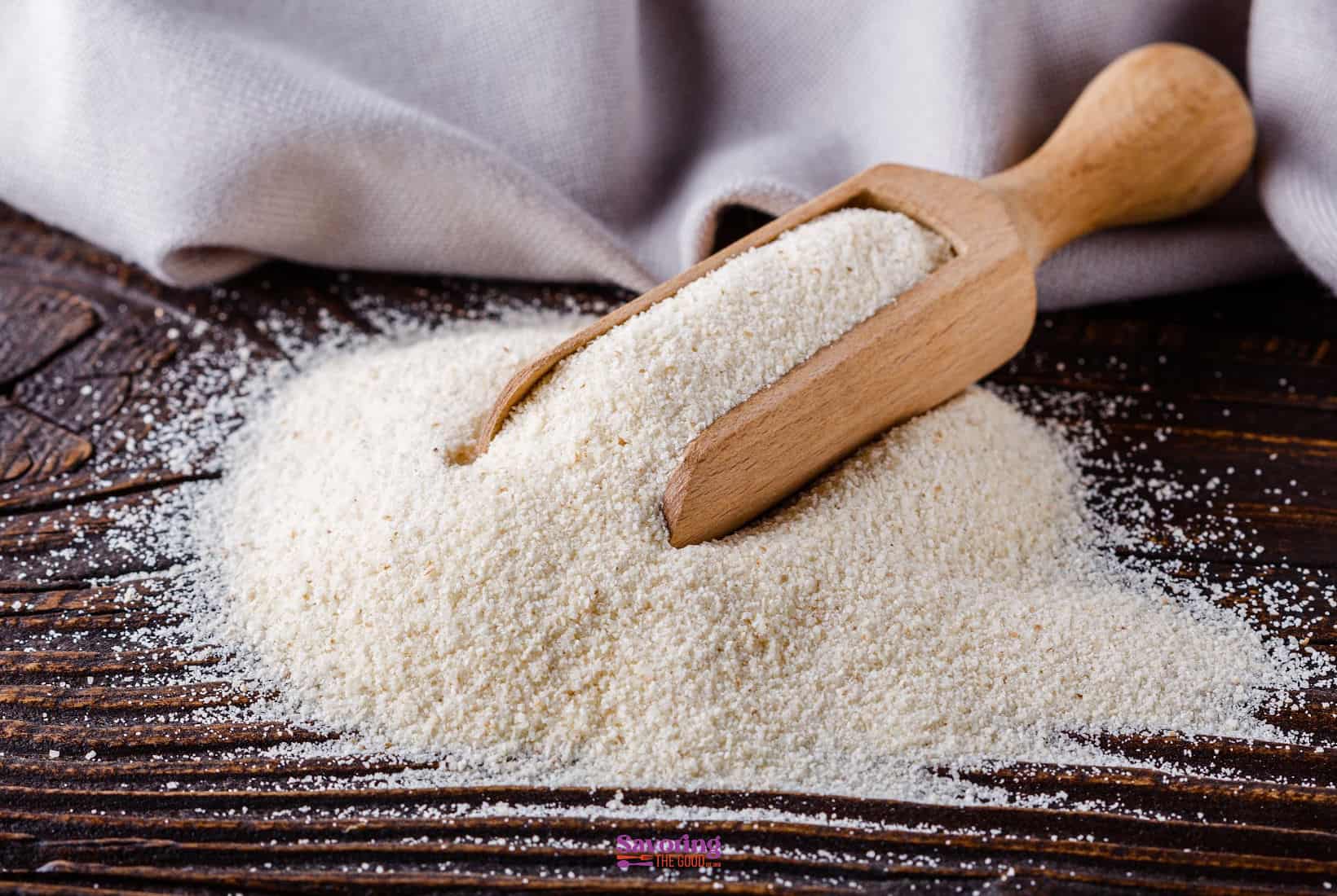 A wooden scoop lies on a pile of fine, white semolina flour, with a sprinkle covering a rustic wooden table.
