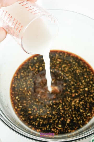 Pouring cornstarch slurry into a bowl of sauce with sesame seeds.