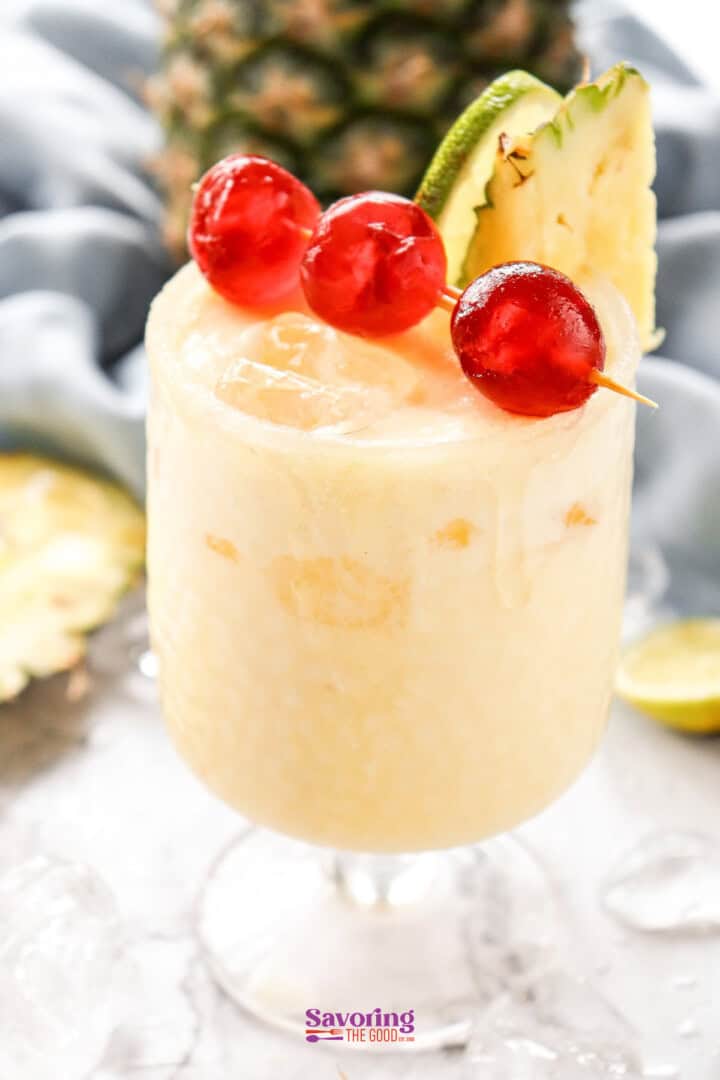 A frozen pineapple pina colada mocktail garnished with cranberries and a pineapple slice, served in a glass on a bed of ice.