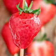 Close-up of a fresh Strawberry tanghulu on a stick, with a glossy appearance and other blurred strawberries in the background.