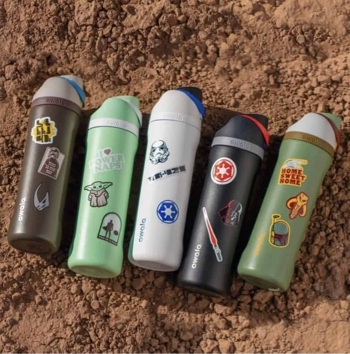 Five reusable water bottles with various Star Wars-themed stickers are lined up on brown soilโunique gifts perfect for Father's Day.