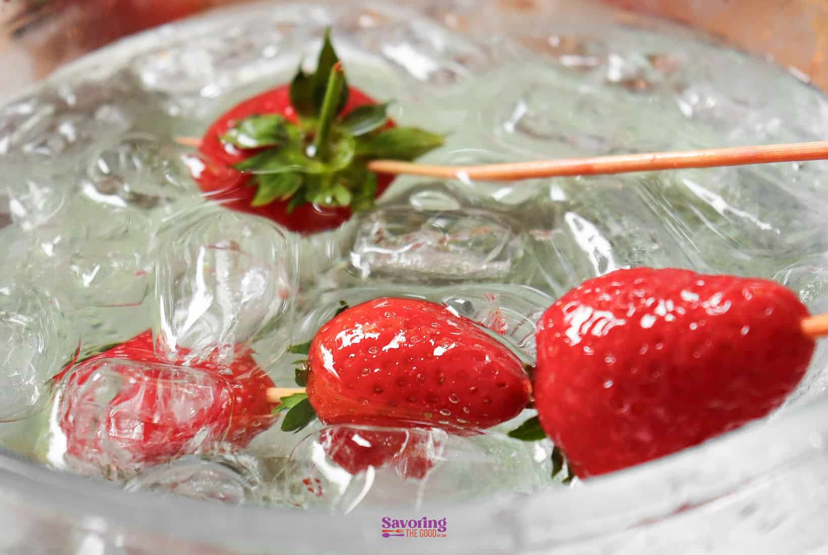 Close-up of Strawberry tanghulu on ice, with a toothpick and water droplets visible on the strwaberries.