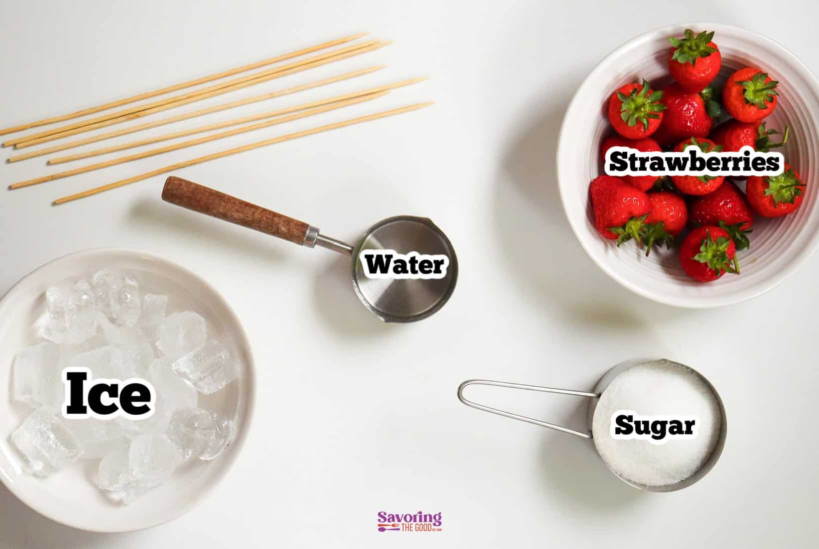 Top view of ingredients for a recipe, including strawberries, water, sugar, and ice, each labeled accordingly, with skewers to the side.