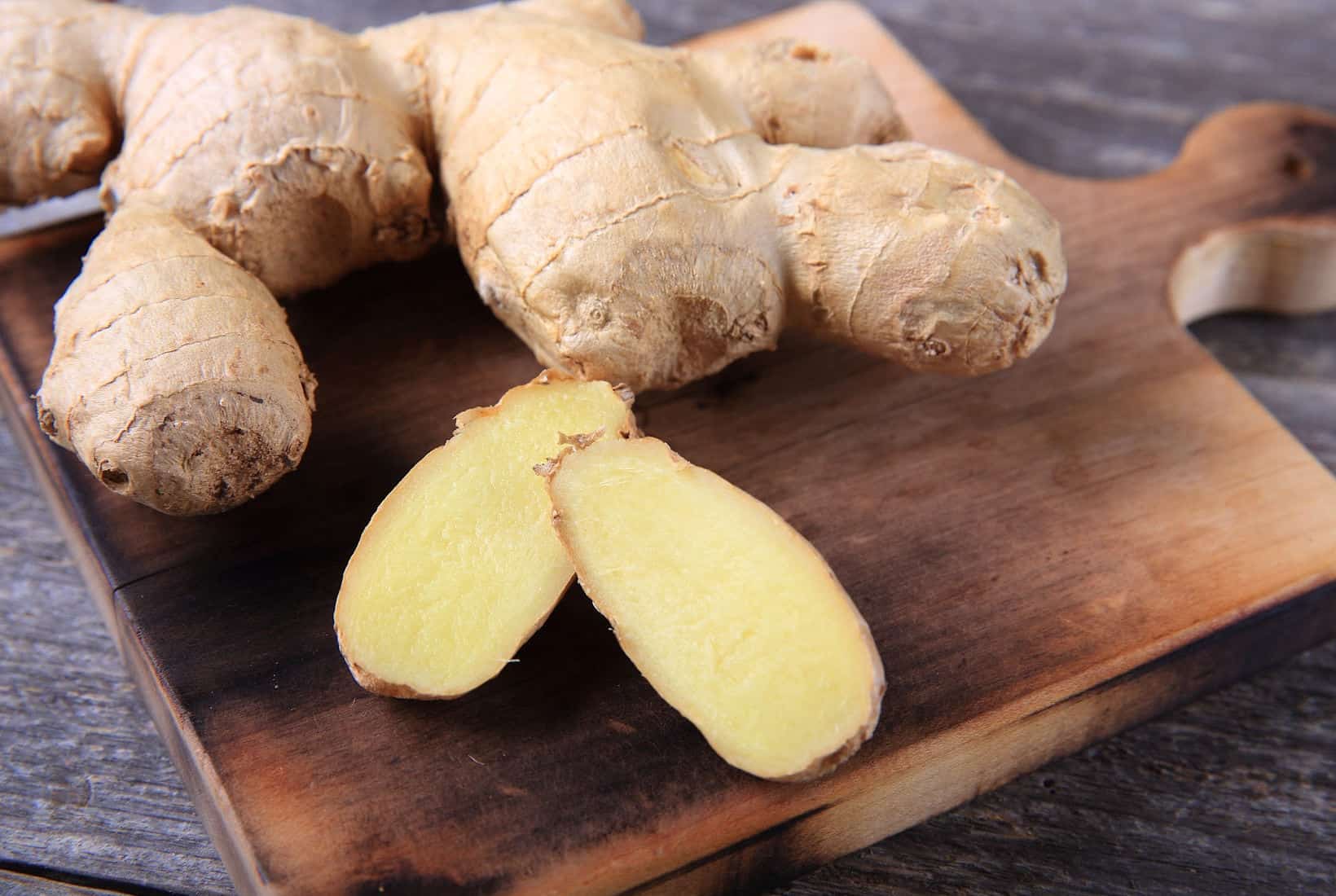 Fresh ginger root and two slices on a wooden cutting board.