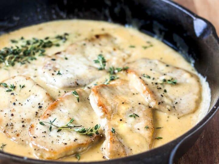 Chicken breasts cooked in a creamy sauce, garnished with fresh thyme, served in a black cast iron skillet on a wooden surface-a perfect inspiration for those searching for flavorful Thin Pork Chop Recipes.