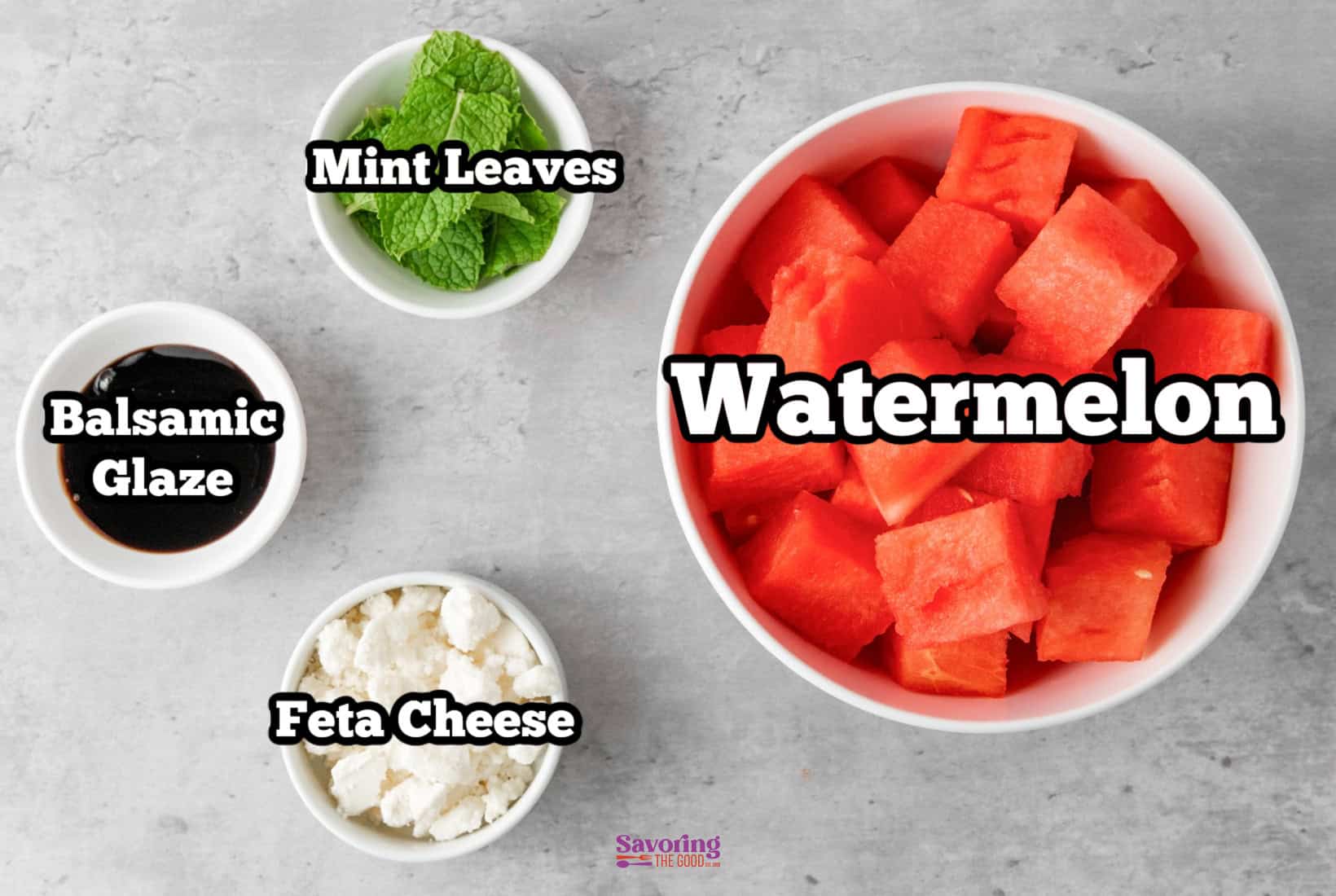 Image showing labeled ingredients for a dish: watermelon chunks in a bowl, mint leaves, balsamic glaze in a cup, and feta cheese crumbles in another cup.