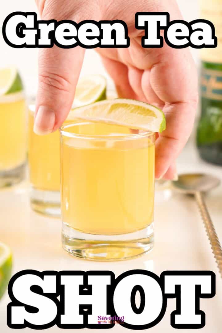 A hand holds a shot glass filled with green tea shot, topped with a lime wedge. Other similar shot glasses and a bottle are visible in the background.
