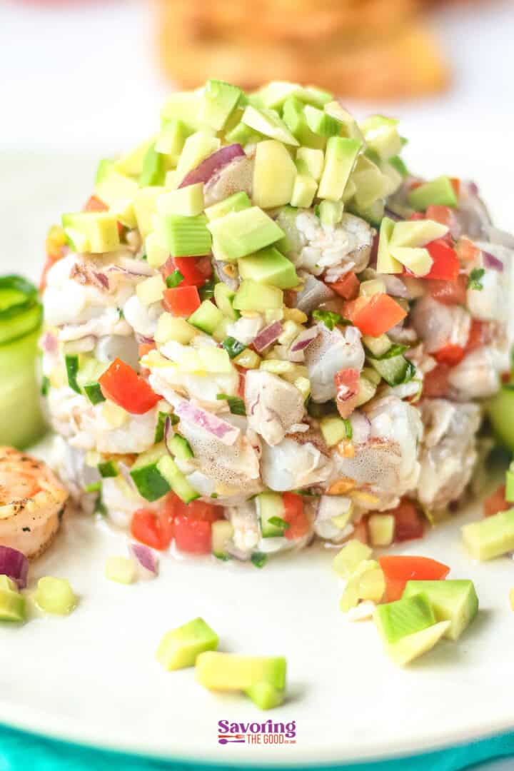 A dish of ceviche topped with diced avocado, red onion, and tomato is served on a white plate.