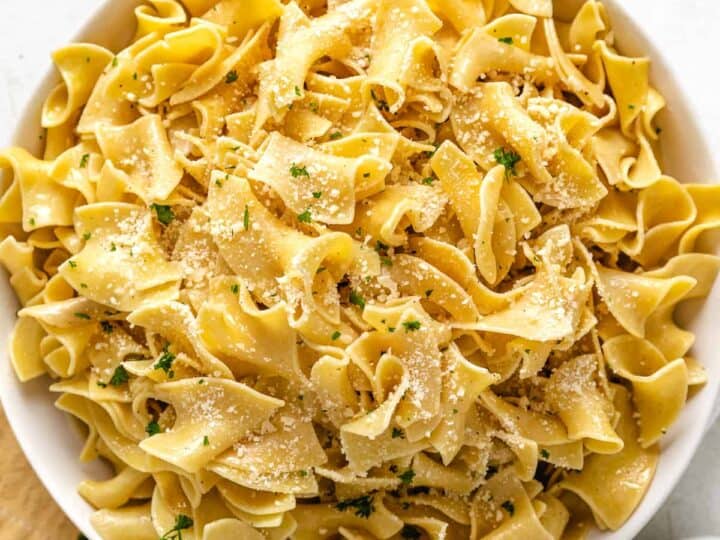 A bowl of cooked egg noodles topped with grated Parmesan cheese and garnished with chopped parsley-an ideal side when deciding what to serve with chicken drumsticks.