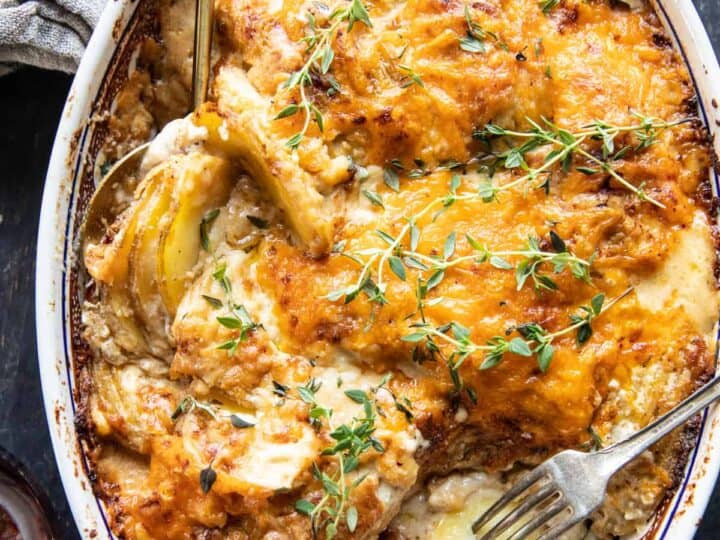 A baked gratin dish with golden, melted cheese on top, garnished with fresh herbs, makes a delicious side when wondering what to serve with chicken drumsticks, with forks placed in the casserole.