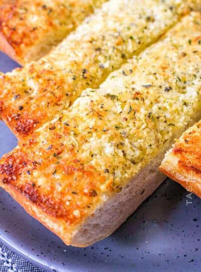 Three thick slices of toasted garlic bread topped with herbs and melted cheese are arranged on a gray plate-perfect for what to serve with chicken drumsticks.