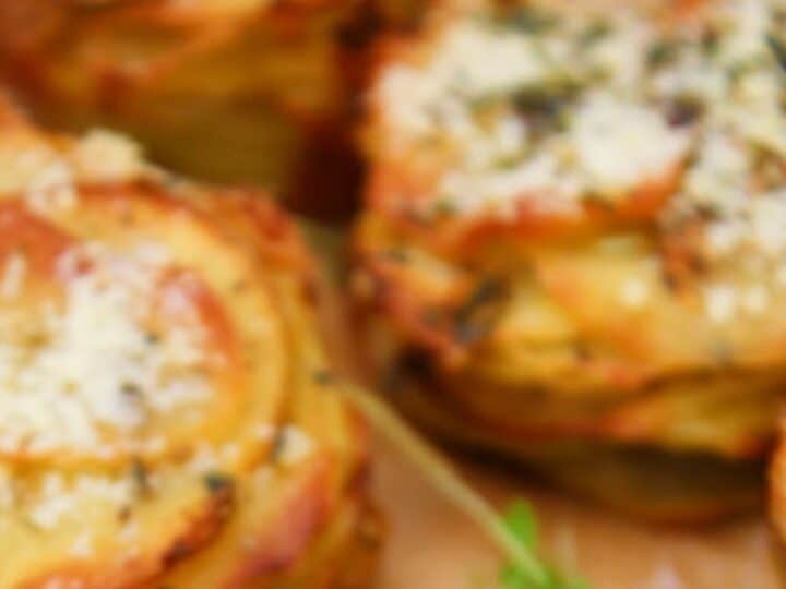 Close-up of baked potato stacks topped with herbs and grated cheese, resting on a wooden surface-a delicious idea for what to serve with chicken drumsticks.